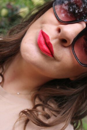 A woman wearing sunglasses and sporting a bold red lipstick from KVD Beauty's Everlasting Liquid Lipstick line.